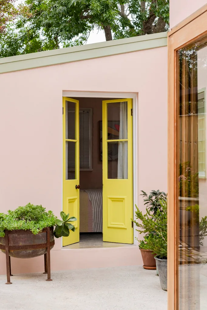 A pink house with a yellow door and potted plants