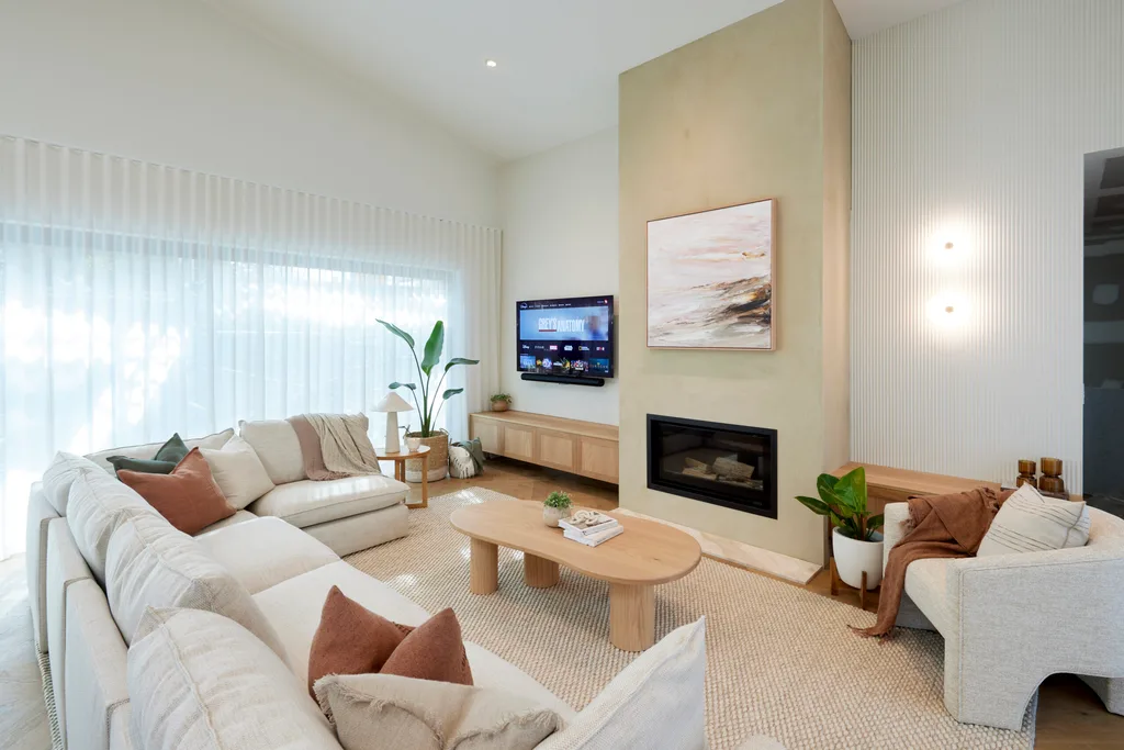 A light coloured living room with a large beige couch, a wall mounted TV and a fireplace