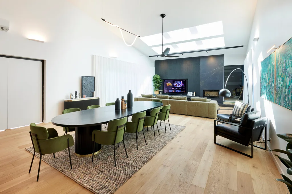 A dining room with a large black dining table, green velvet chairs and black accents.