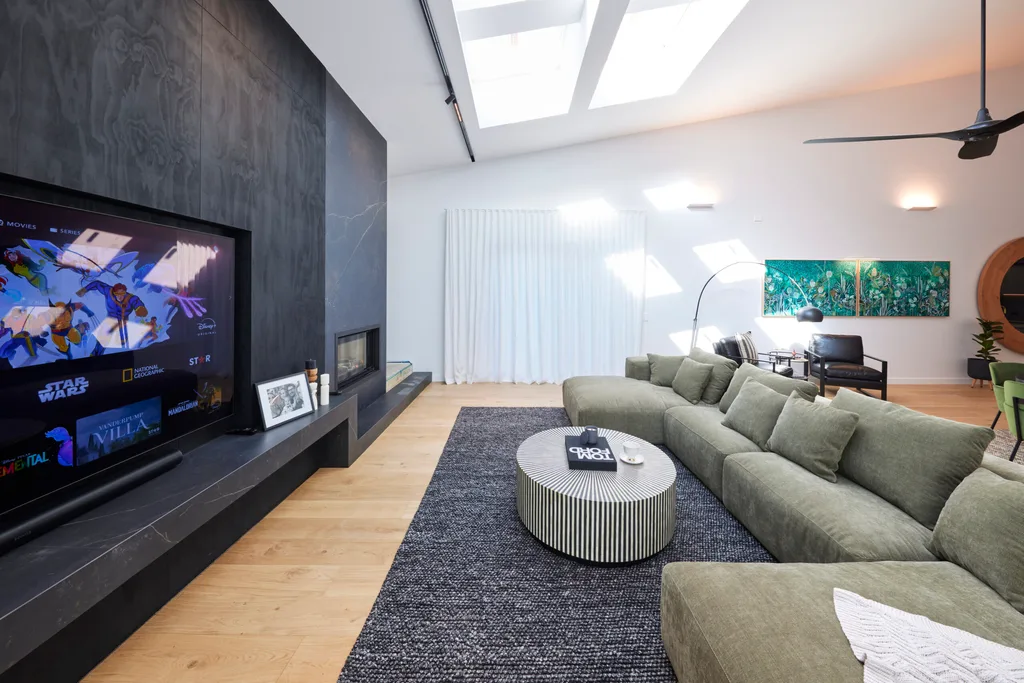 A living room with a black feature wall with in-built fireplace, a large green couch and a black fan.