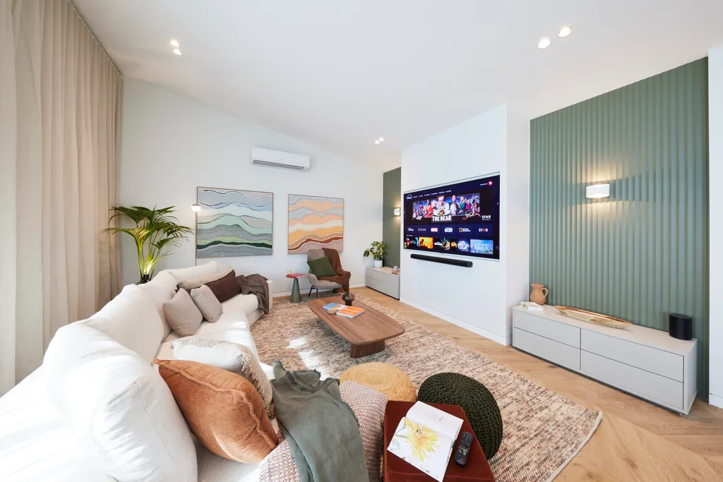 A living room with a beige couch, a large rug and a wall-mounted tv