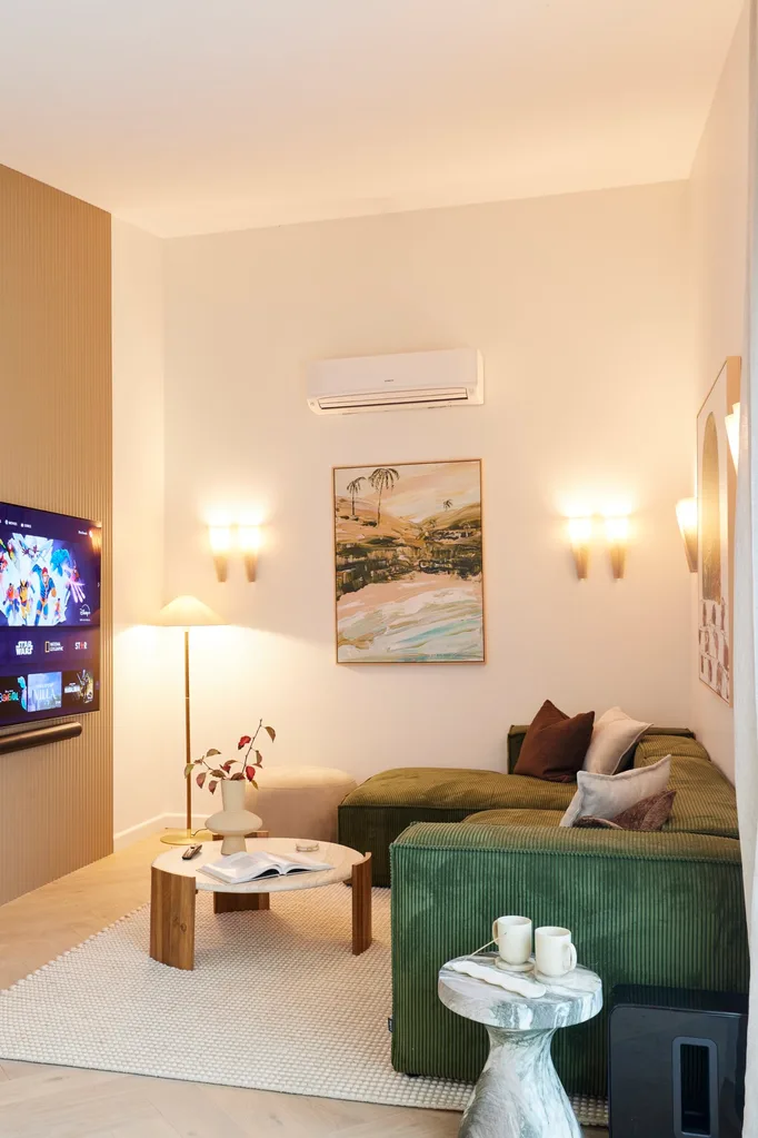 A lounge space with wall sconces, a green corduroy lounge and a wall-mounted TV