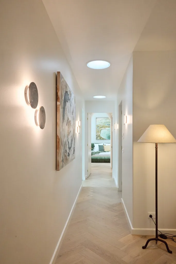 A hallway with wall sconces and skylights