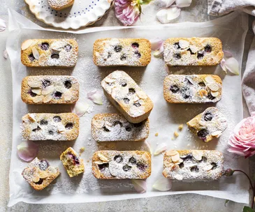 A tray of blueberry friands with icing sugar and roses