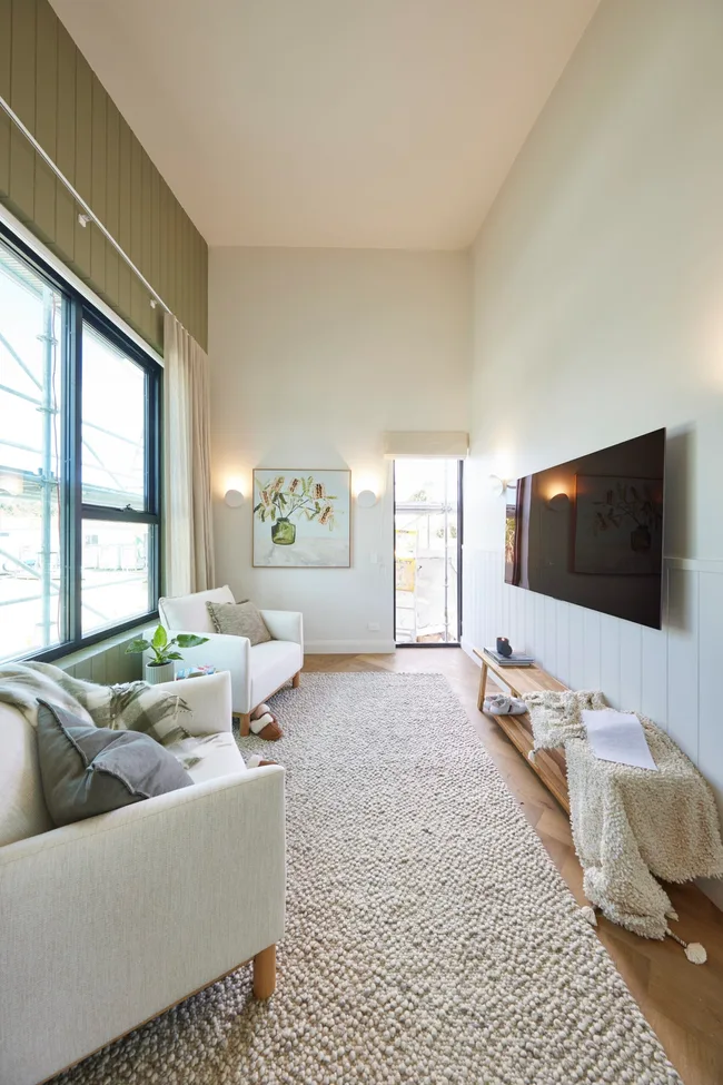 A lounge space with a large beige rug, green feature wall and two white armchairs