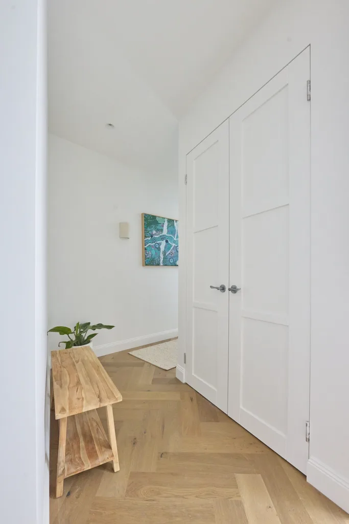 A white hallway with a timber bench seat and plant