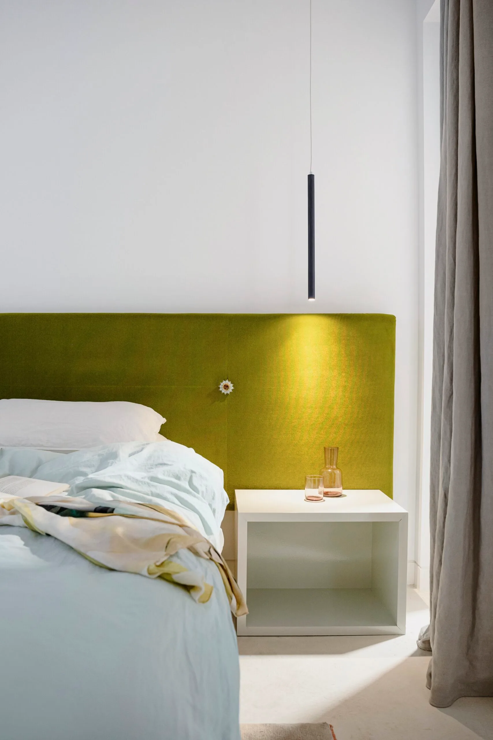 A bed with a green built-in wall feature, blue sheets and a cube-style bedside table