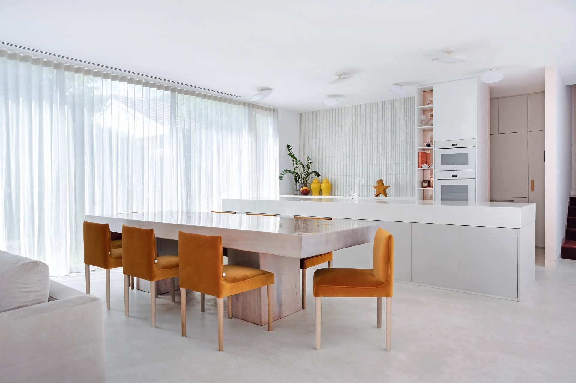 An open-plan kitchen and dining with orange chairs and concrete floors