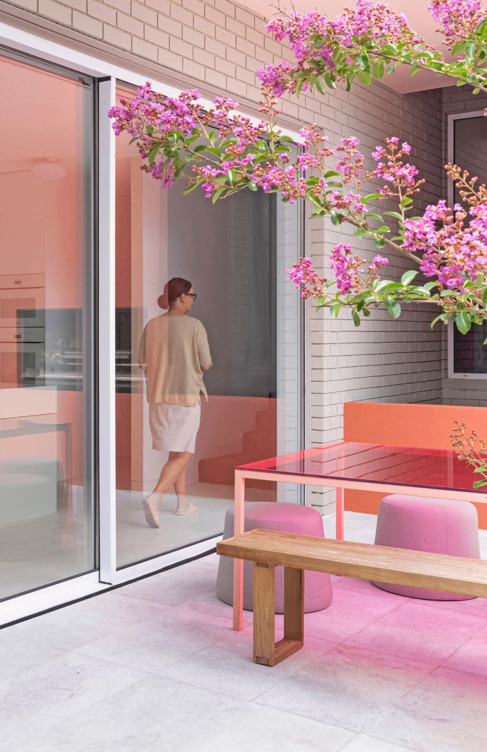 An outdoor dining set with a pink glass-topped table and a tree with pink flowers