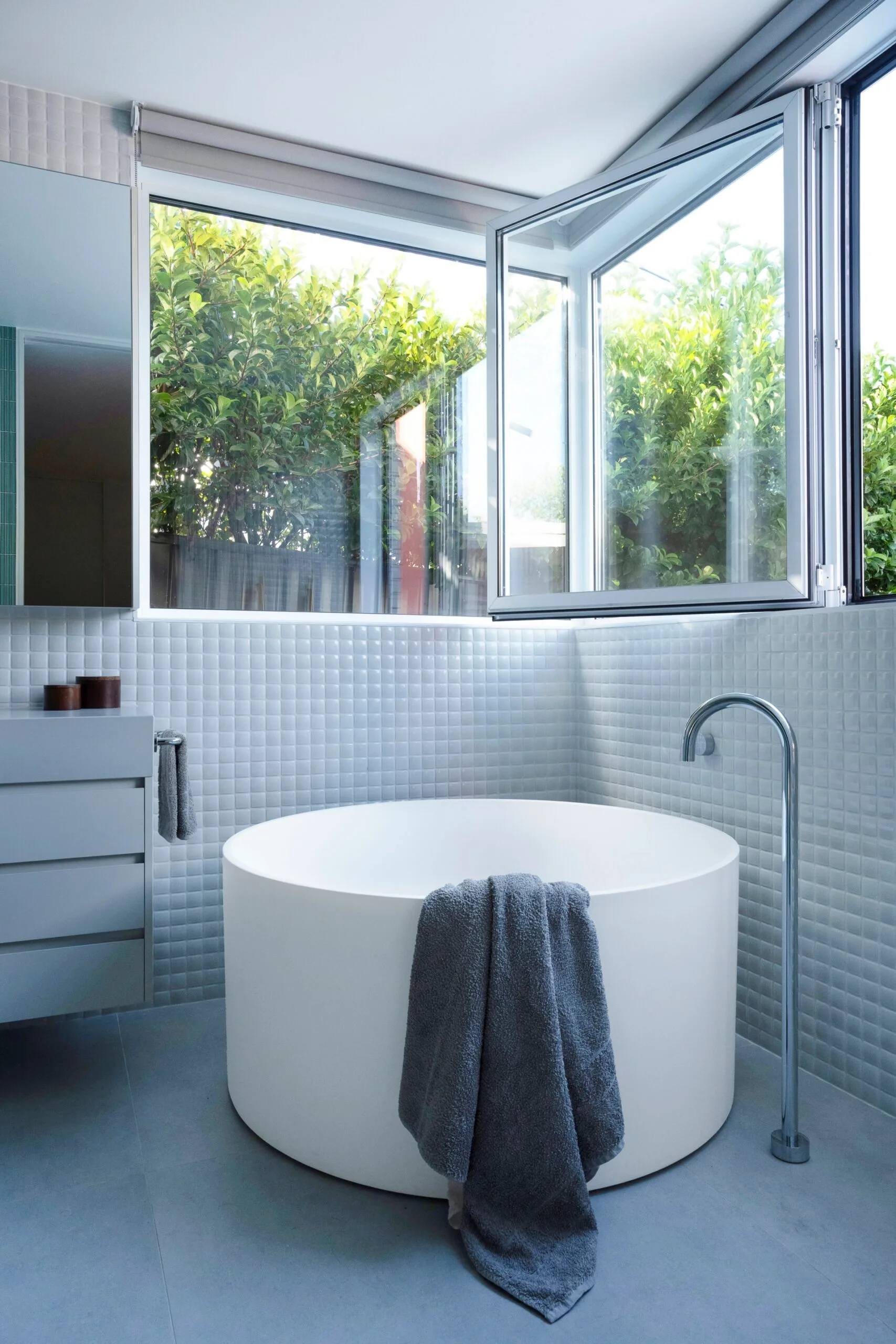 A freestanding circular bath tub in a grey and white bathroom with large square windows