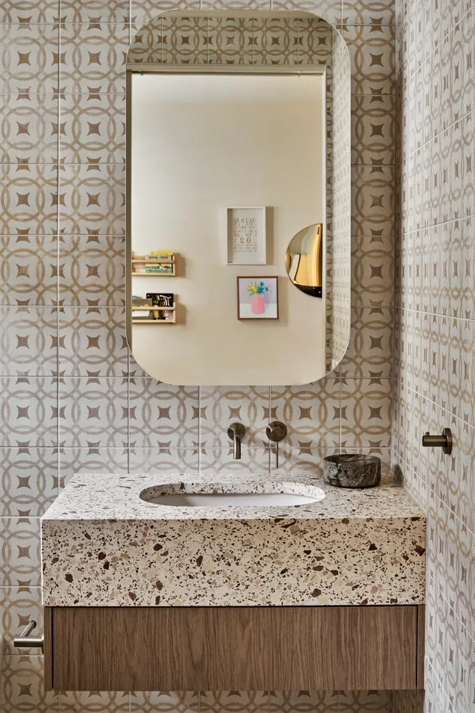 A neutral-toned bathroom with a terrazzo benchtop, striking tiling and a curved mirror