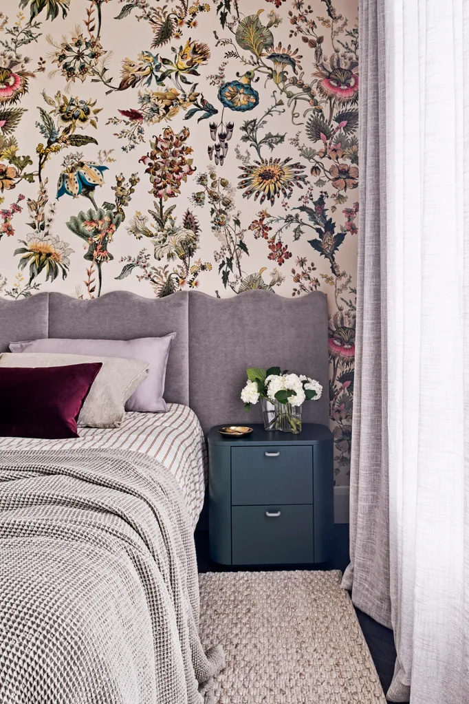 A cosy bedroom with floral wallpaper and a grey bedhead