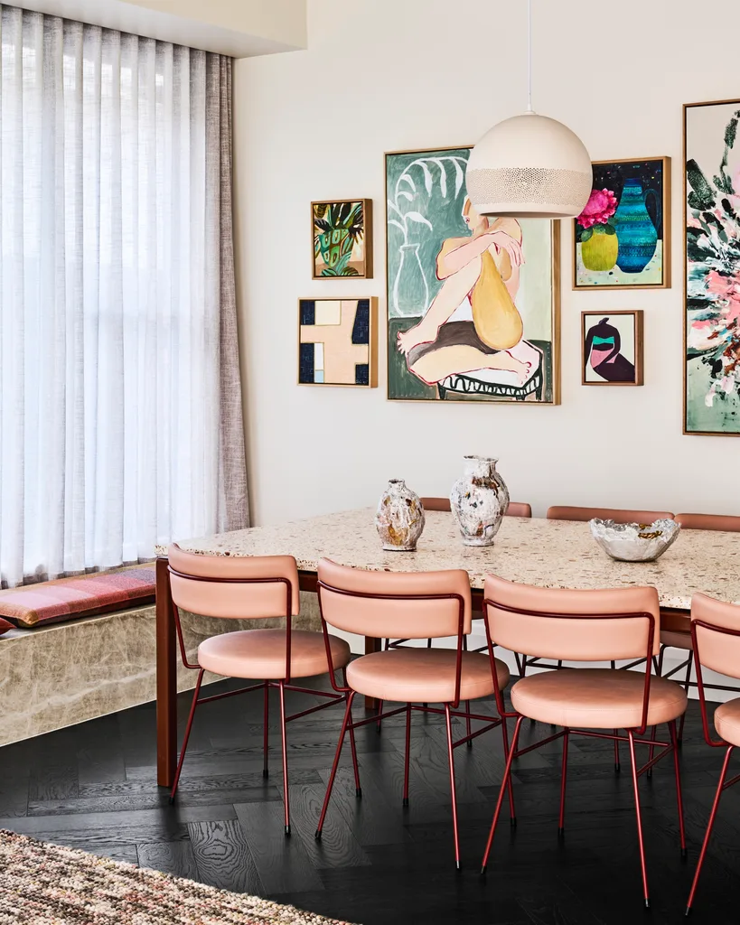 A dining room with pink dining chairs and a gallery wall of colourful paintings