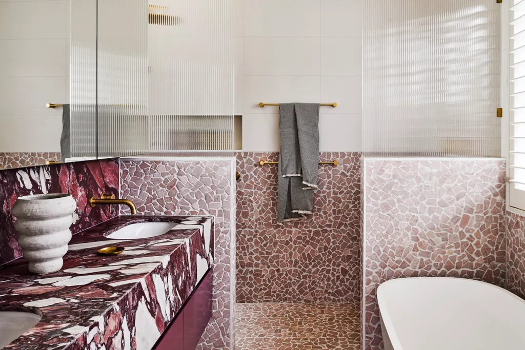 A pink and white bathroom with a stone benchtop and mosaic shower
