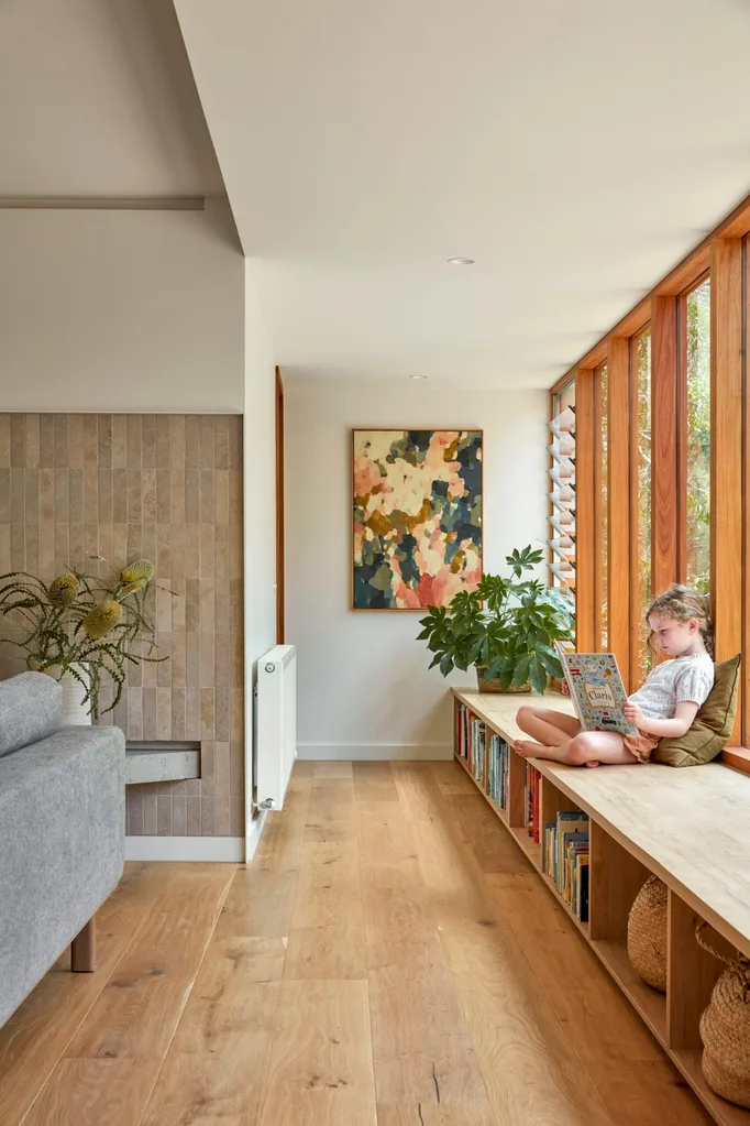 A child reads a book while sat on an in-built shelving unit and window seat