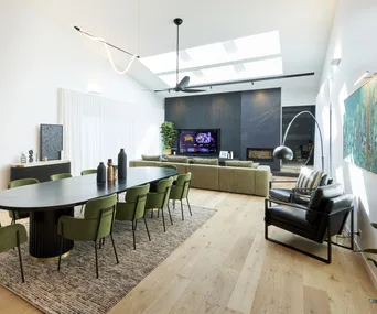 A dining room with a large black dining table, green velvet chairs and black accents.