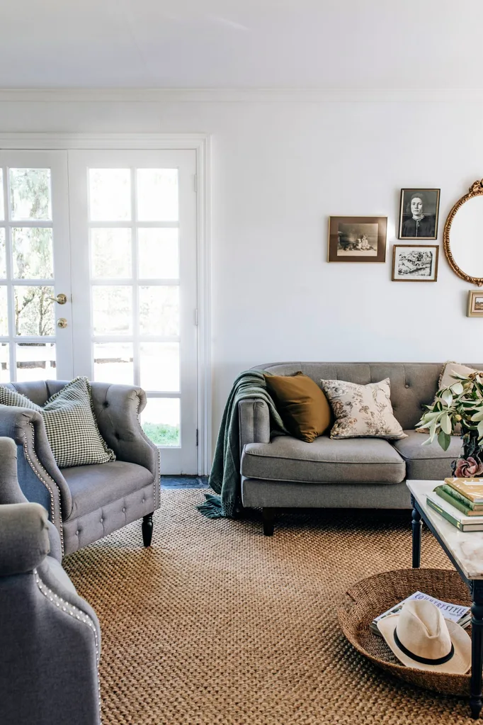 A living room with grey upholstered couches, a large brown rug and a small gallery wall with gold frames.