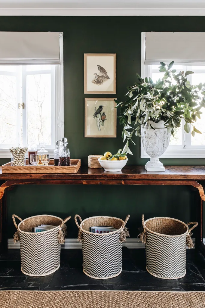 An antique wooden side table decorated with a drinks tray, lemons and a leafy display, set against a deep green wall.