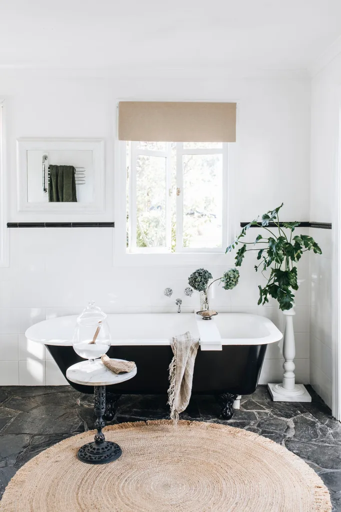 A black bath in a white bathroom with a jute rug