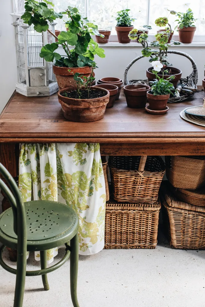 A wooden desk with pot plants on top and wicker baskets underneath.