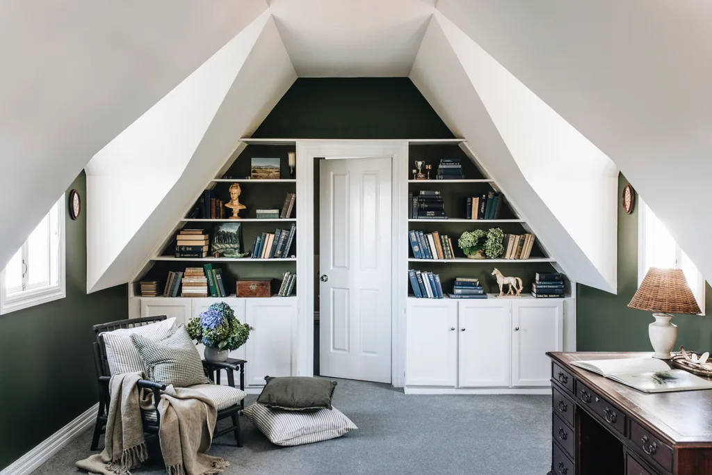 An attic room with a sloped white ceiling, dark green walls and a bookshelf filled with antique treasures.