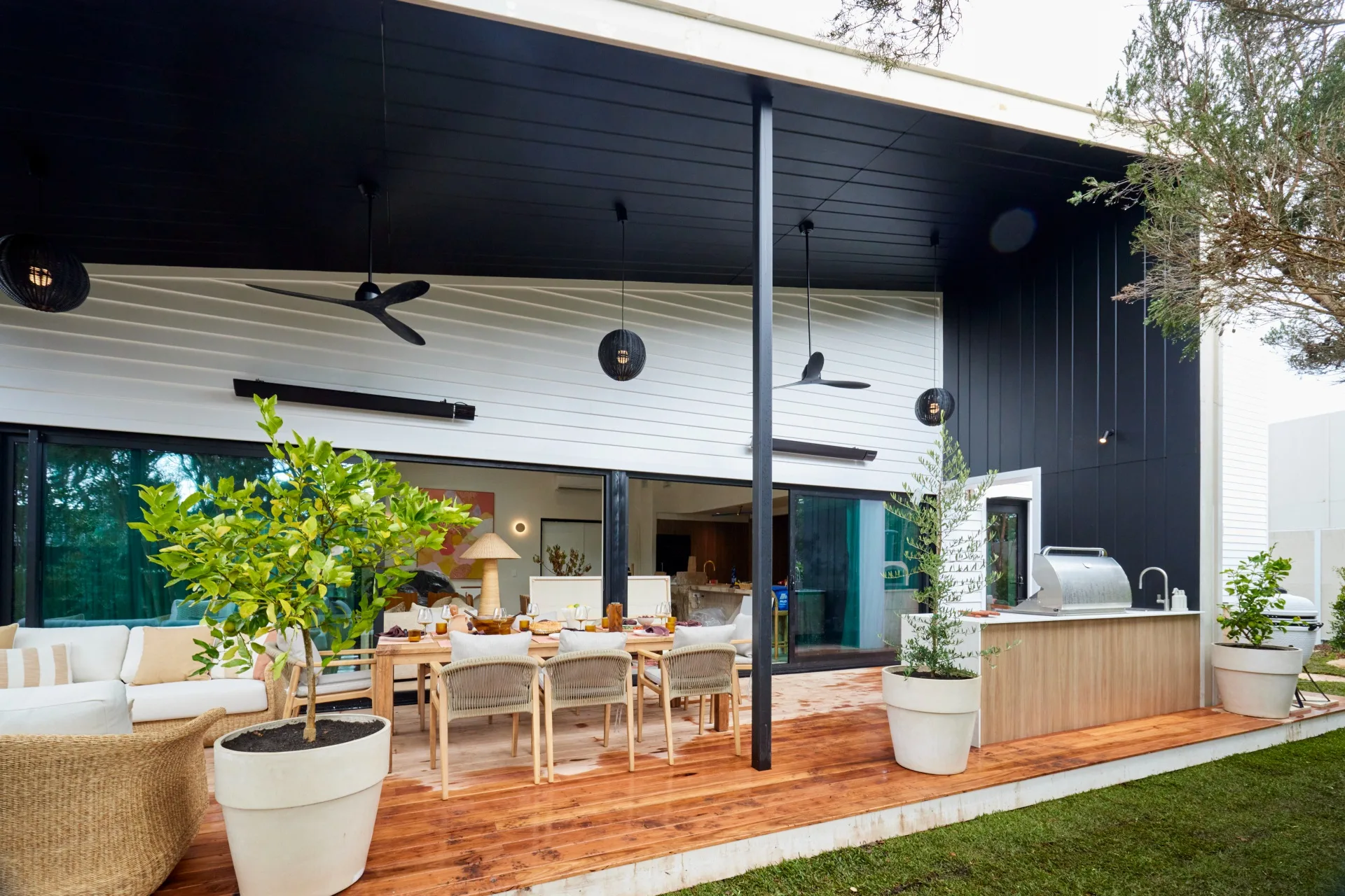 A large covered deck in Courtney and Grant's home on The Block. The area features an 8-seater dining table, an outdoor barbecue area and a lounge area.