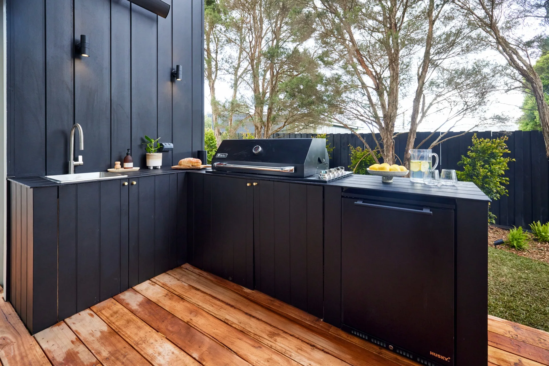 A black, panelled outdoor kitchen with a barbecue and a sink.