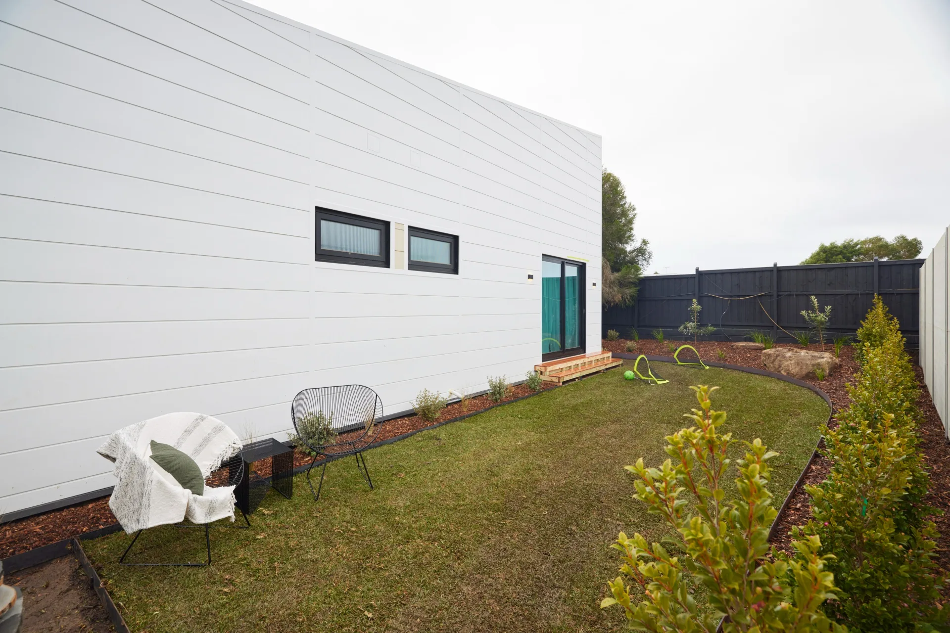 The backyard of a white coastal home with a lawn and landscaped gardens