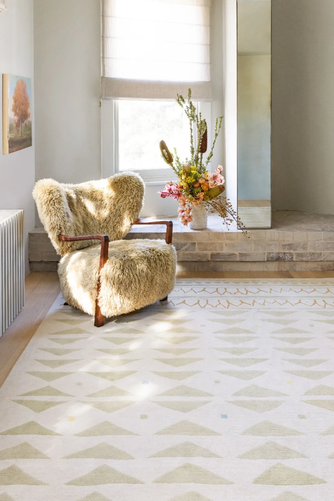 A fluffy chair on a rug near a window and flowers.