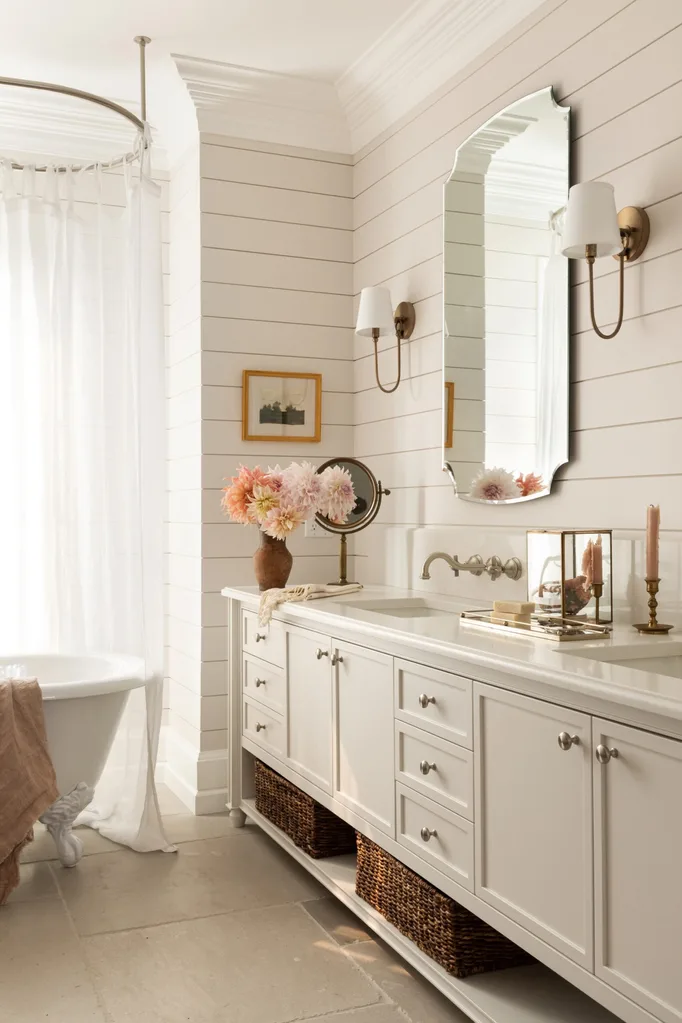 A bathroom with a clawfoot tub, two sinks set into a white vanity and an antique mirror and sconces.