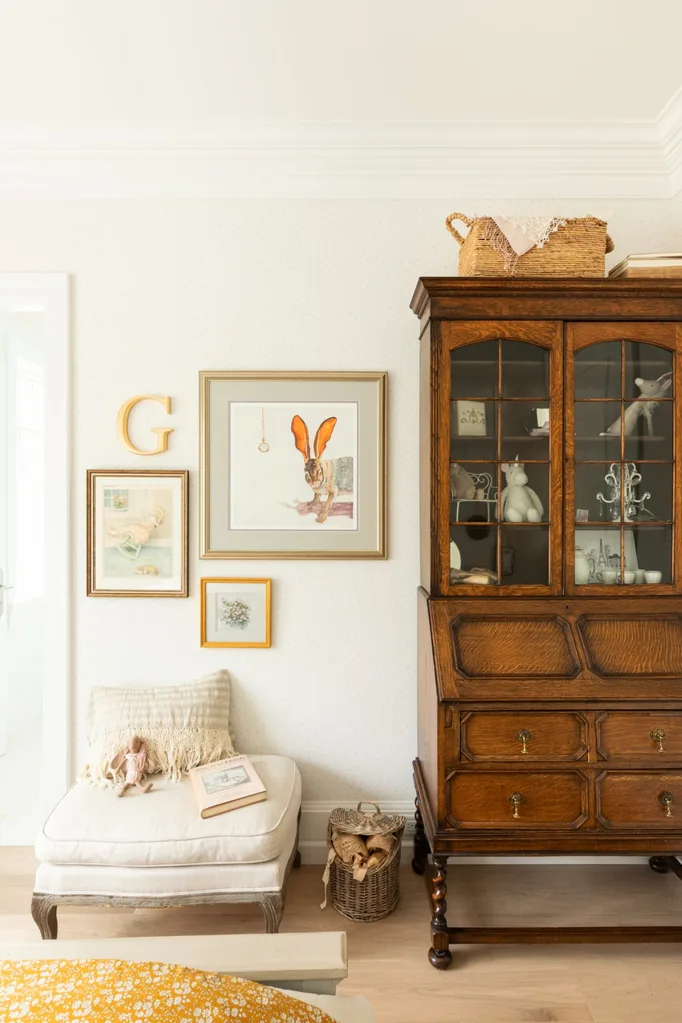 A children's bedroom with a mahogany display cabinet and some gold framed prints.