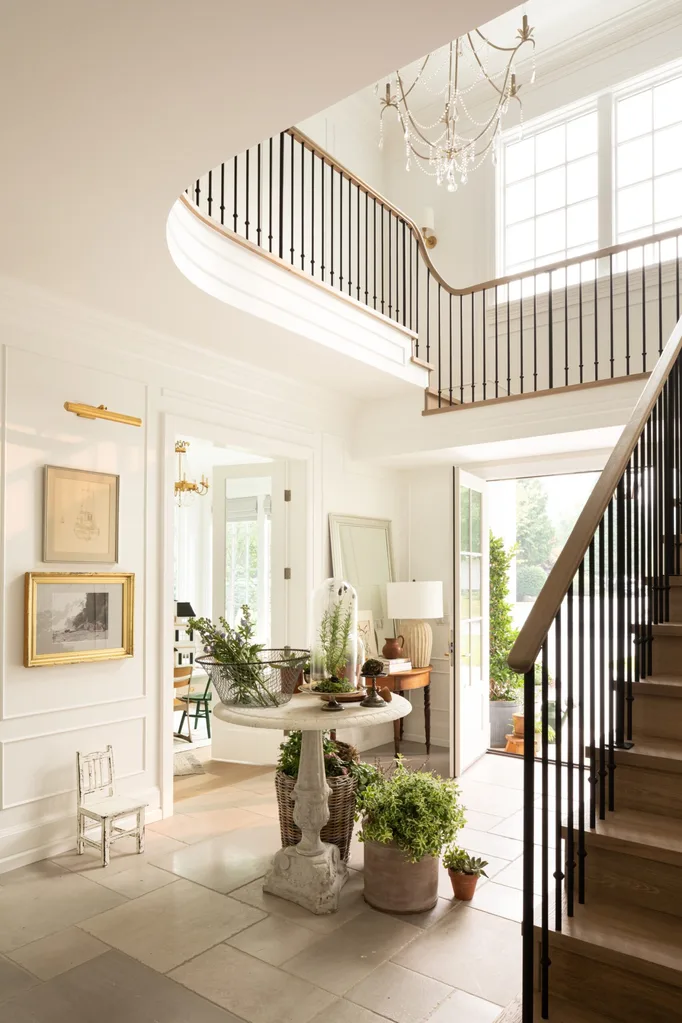 A double-height entryway with a wraparound staircase and a large chandelier.