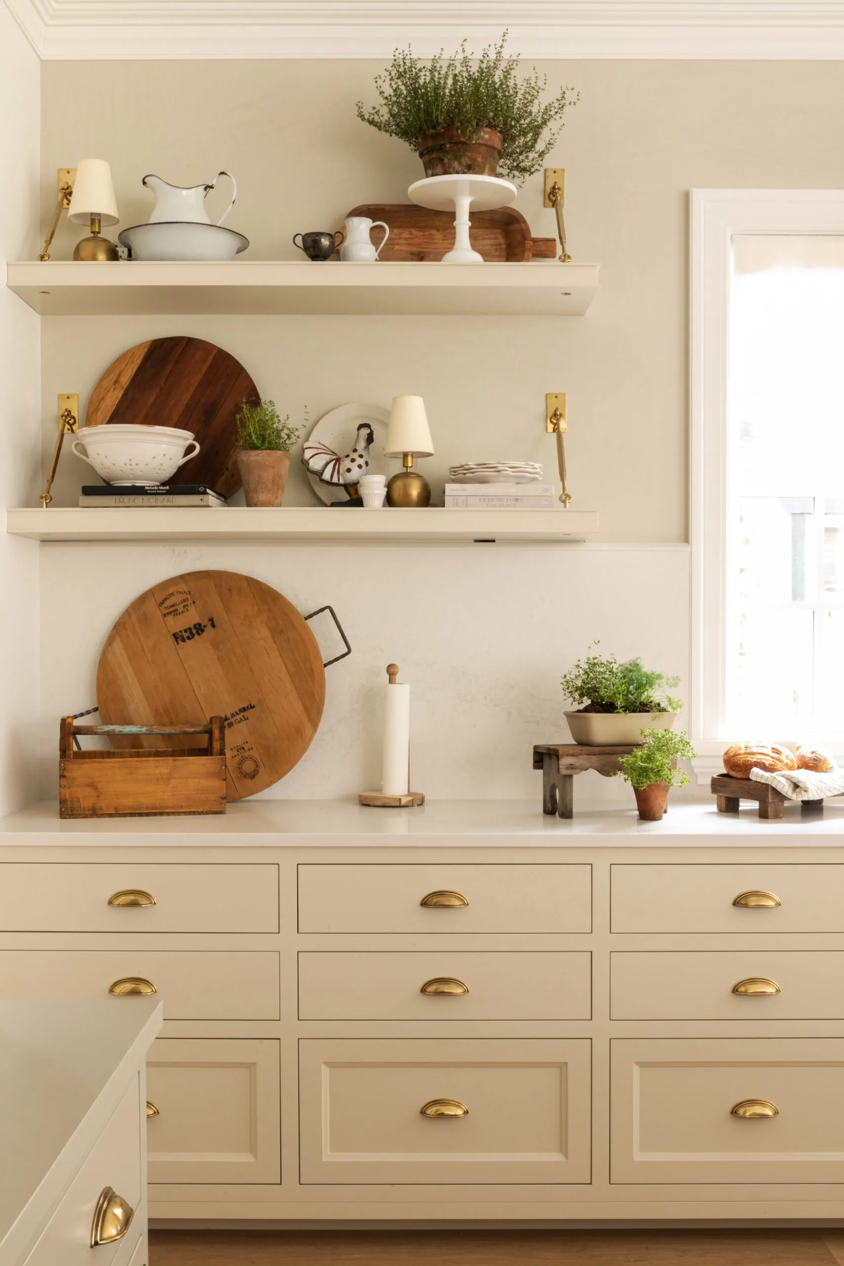 A corner of a white kitchen, with gold drawer pulls and assorted objects on floating shelves.