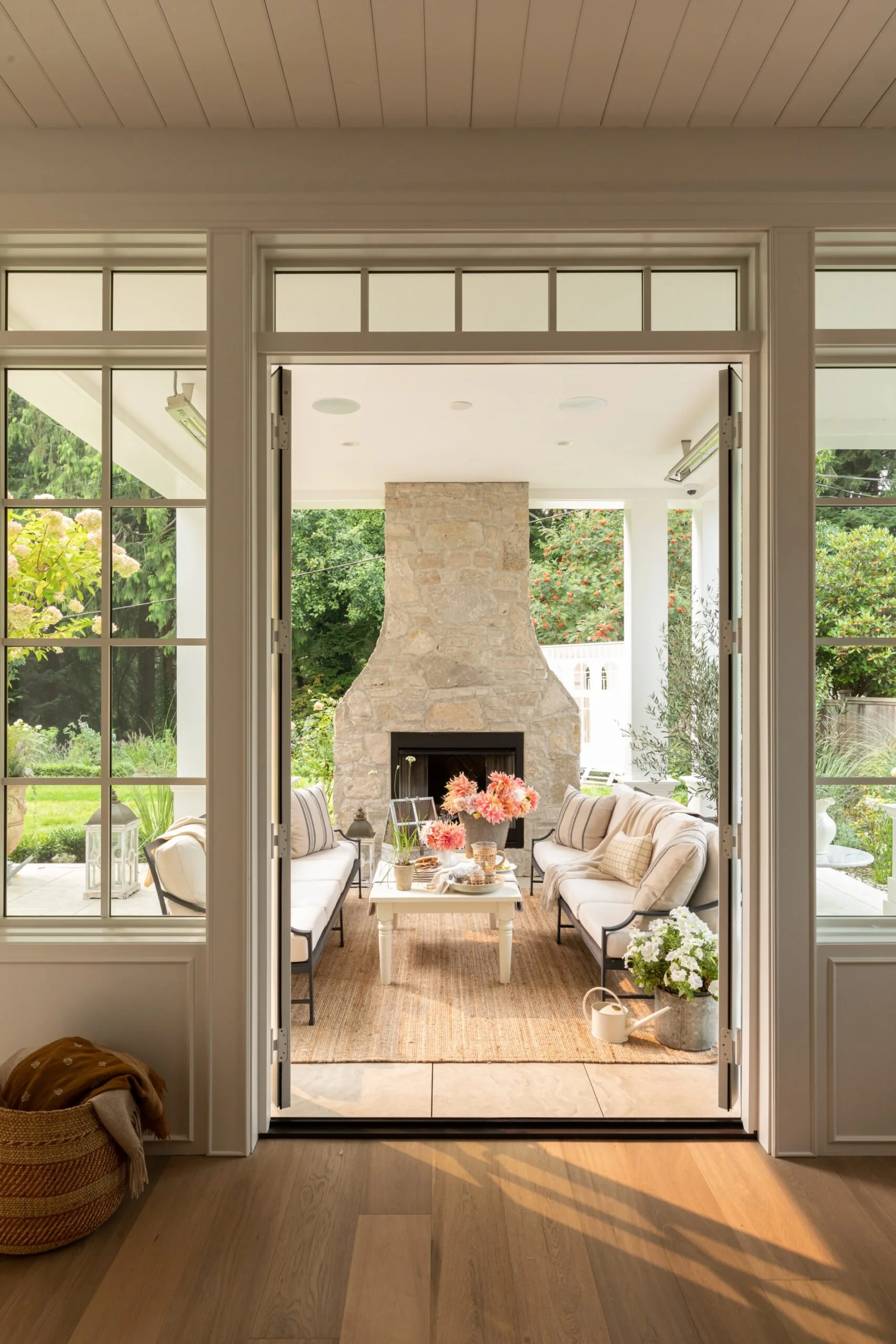 A view through French doors to a covered, outdoor entertaining area with a fireplace and white outdoor couches.