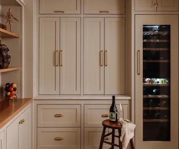 A blush-toned kitchen with gold handles and a large wine fridge