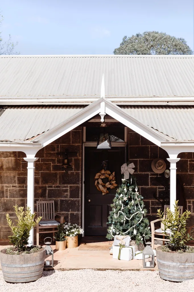 The front porch of a quaint brick home decorated with a Christmas tree, wreath and presents