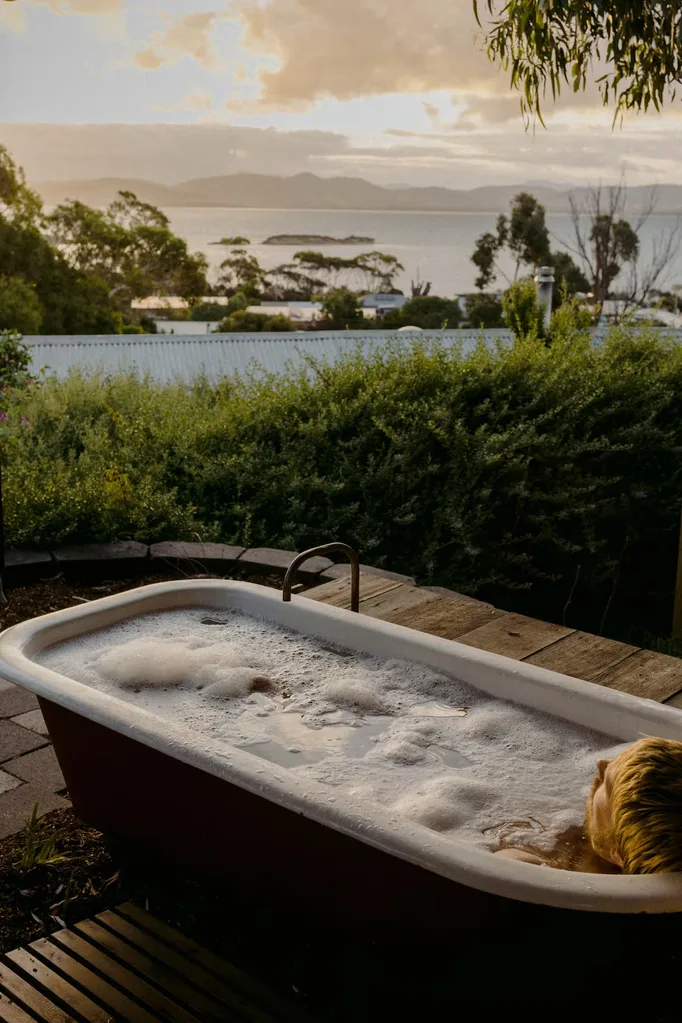 A person sits in an outdoor bathtub overlooking the water