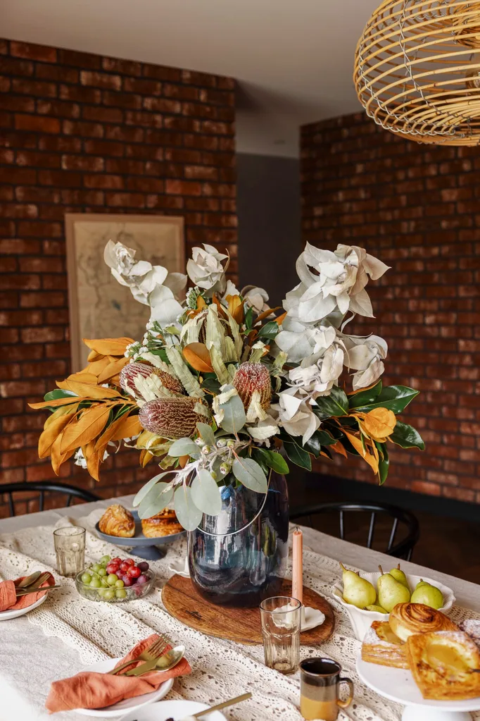 A native floral arrangement on a table with fruit and pastries