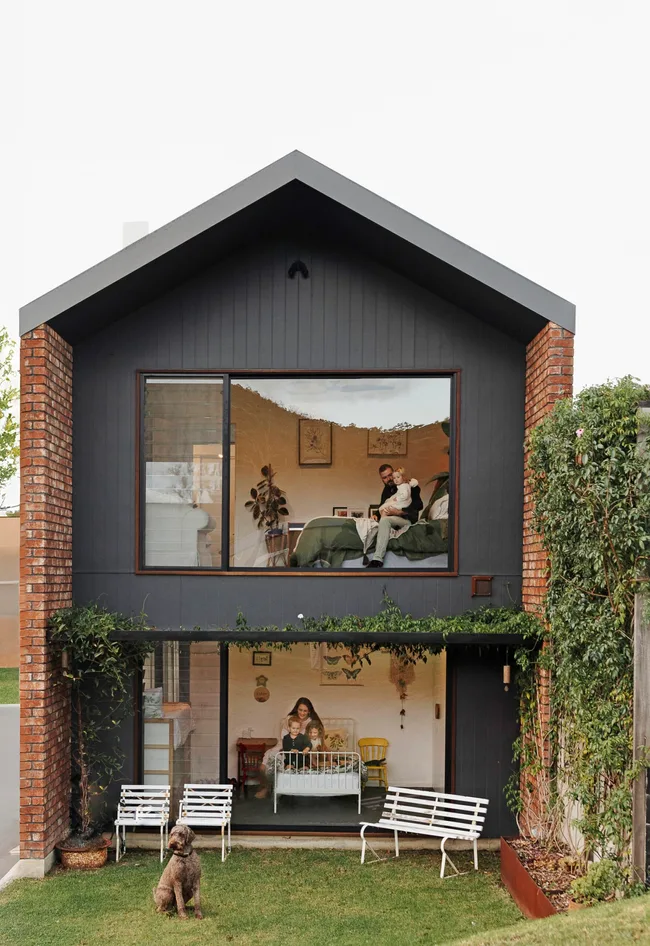 A double-storey family home with large windows and a dog sitting outside on the lawn