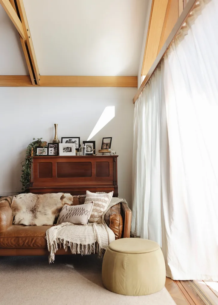 A light and airy living area with a timber upright piano and long white curtains