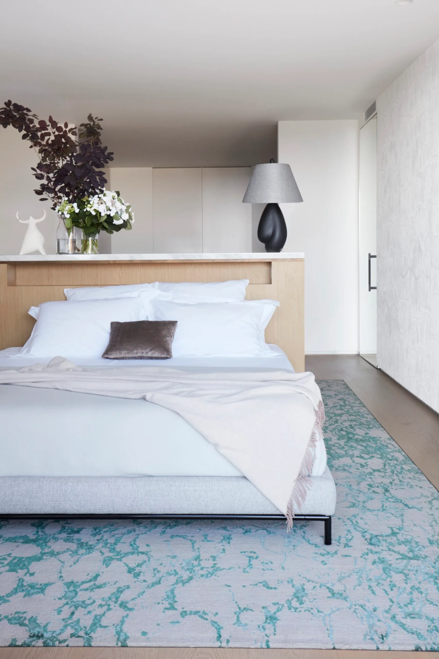 A bedroom with a blue and beige rug and a built-in timber bedhead