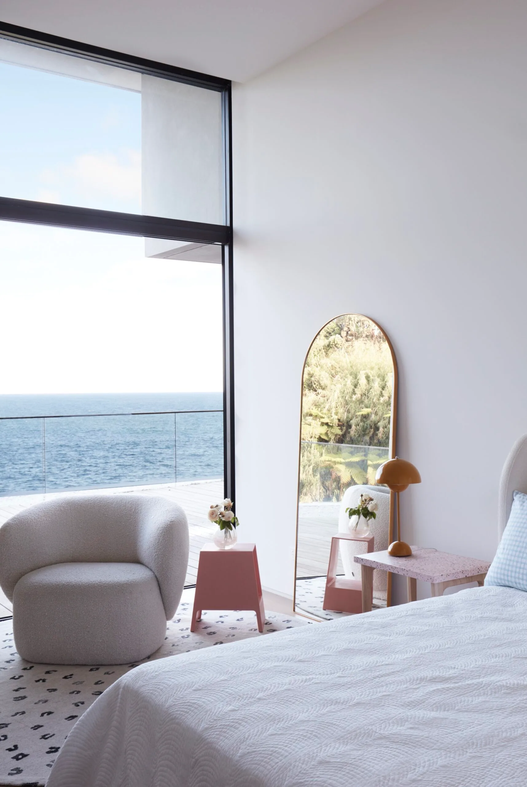 A neutral-toned bedroom with pink accents and an ocean view