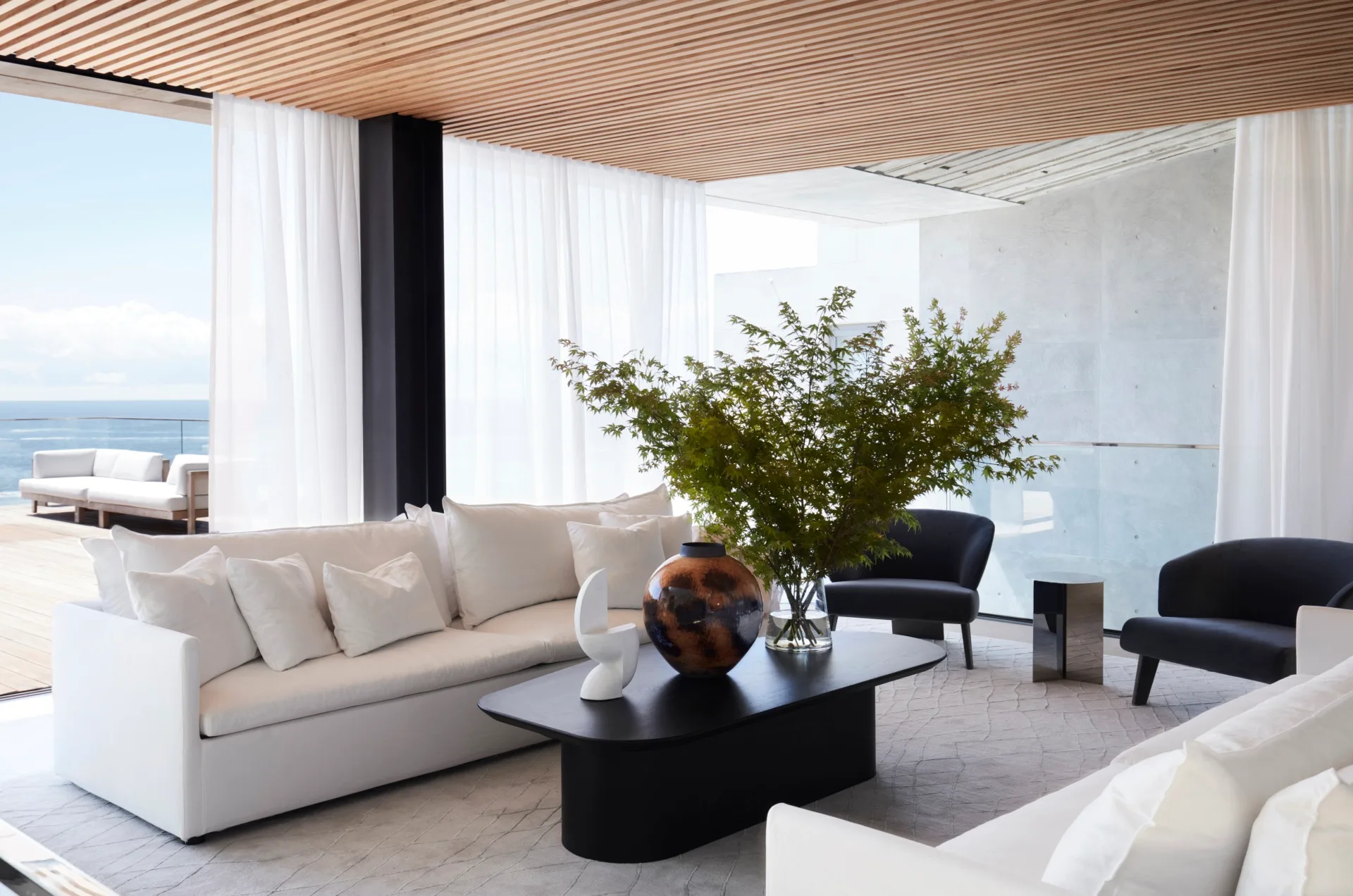 A large living area with white couches looking out onto a sunny balcony overlooking the ocean