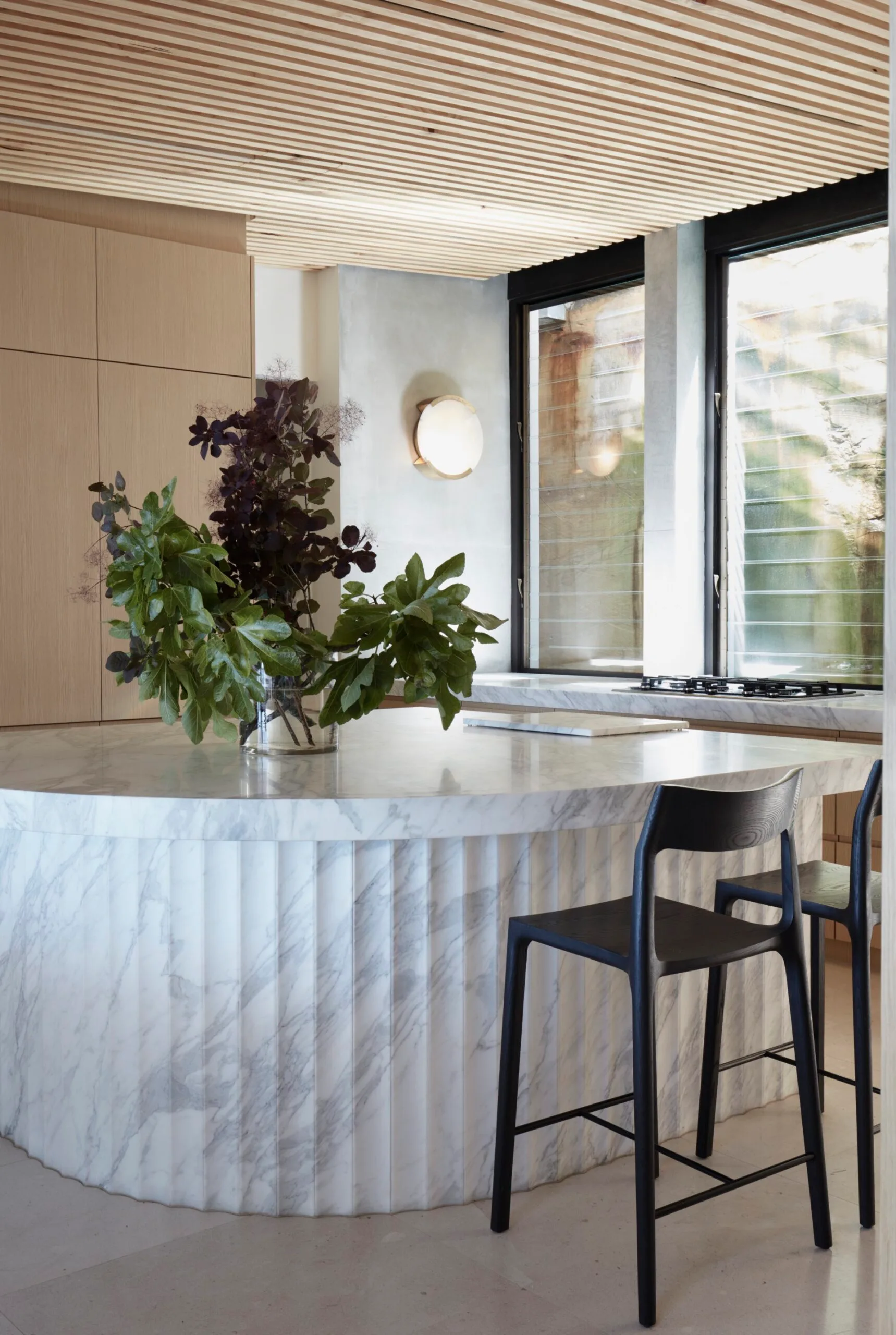 A contemporary kitchen in David Warner home with a curved marble island bench