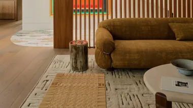Contemporary living room with a brown sofa, wooden slats, abstract artwork, and modern decor elements.