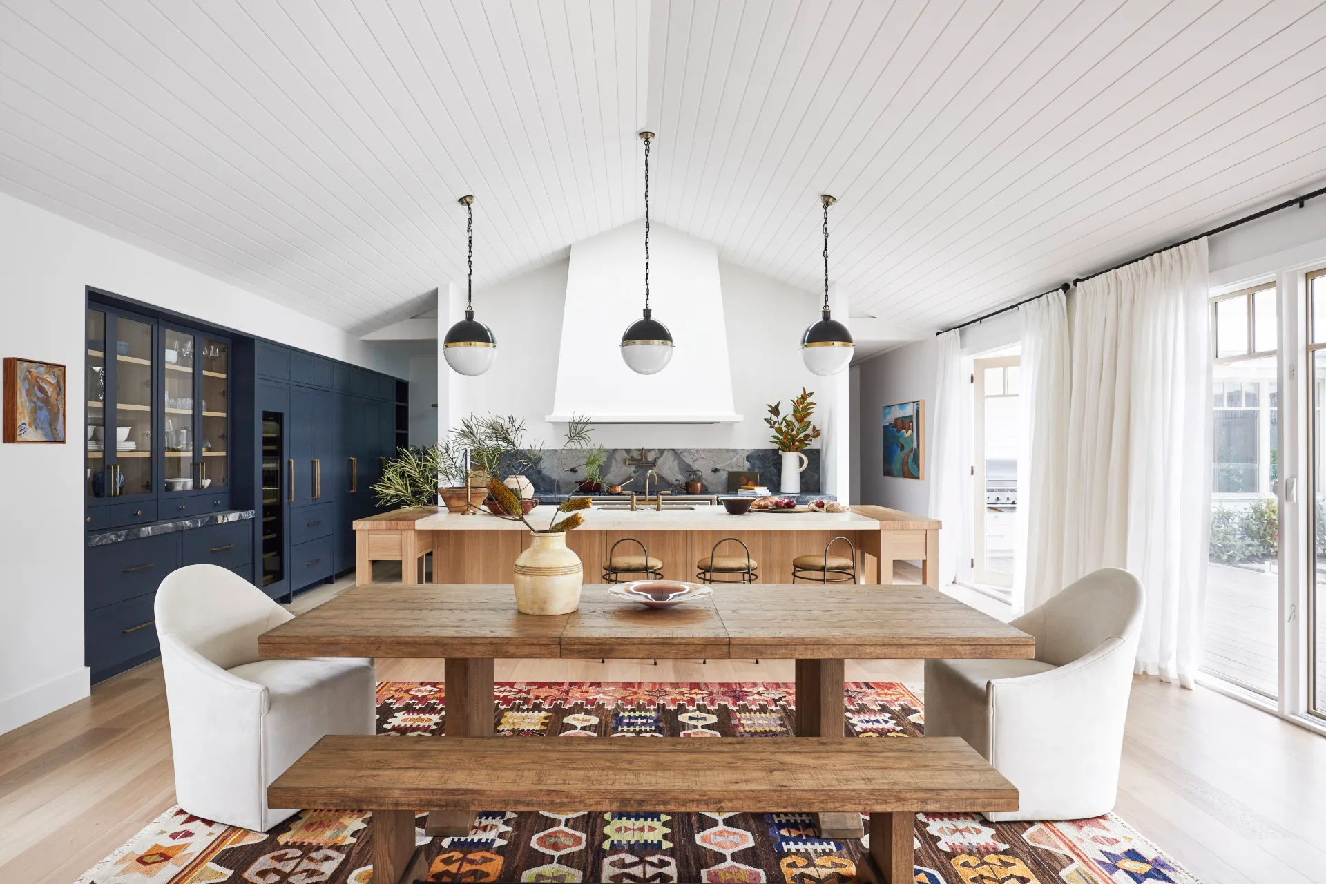 An open-plan living, dining and kitchen area featuring blue cabinetry and timber furnishings