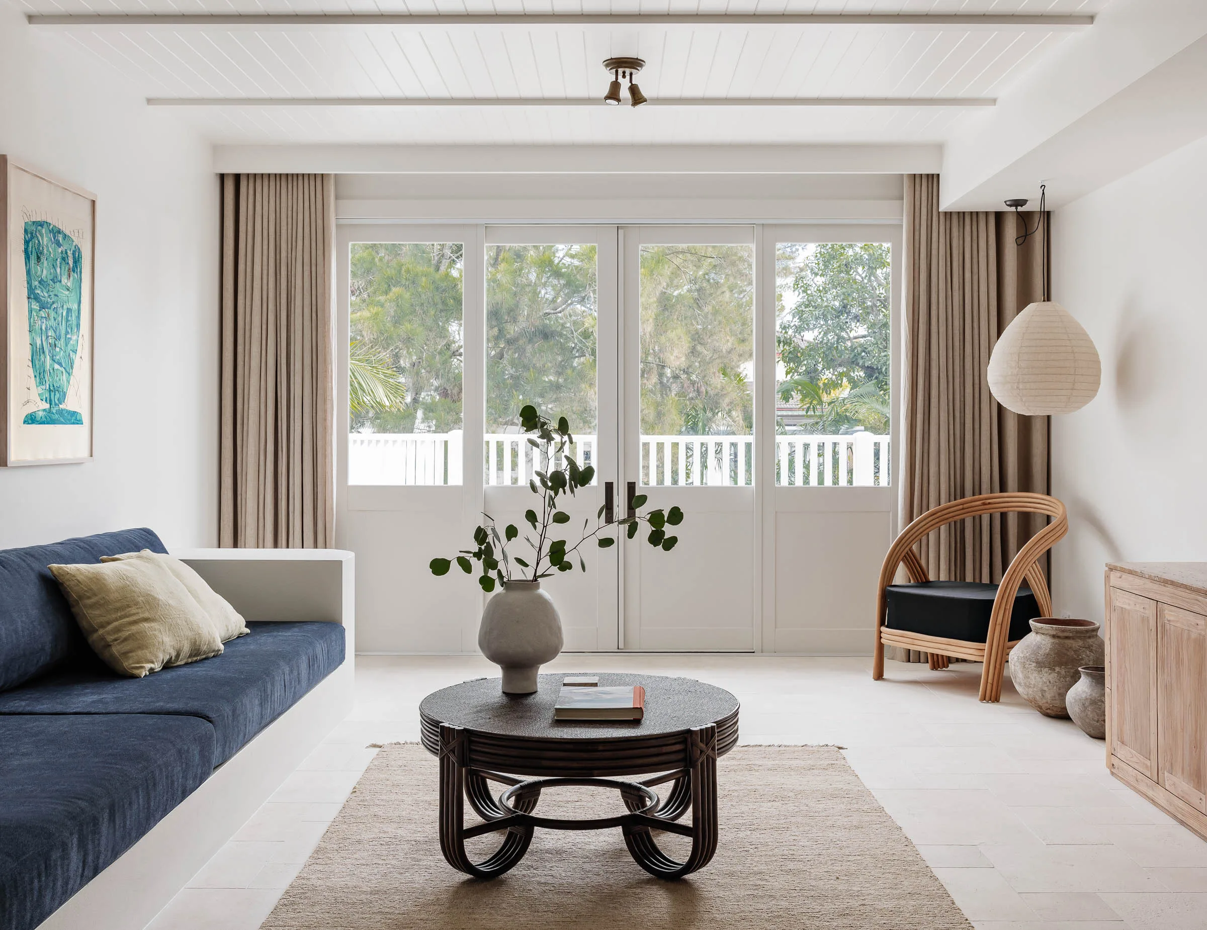 A living room with large white sliding doors, neutral curtains and a blue upholstered bench seat