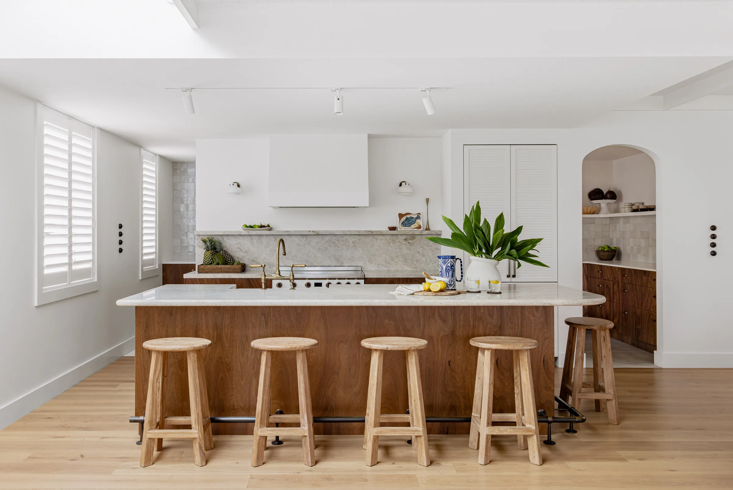 A kitchen with a Taj Mahal stone island bench with wood veneer, a brass footrest and curved details