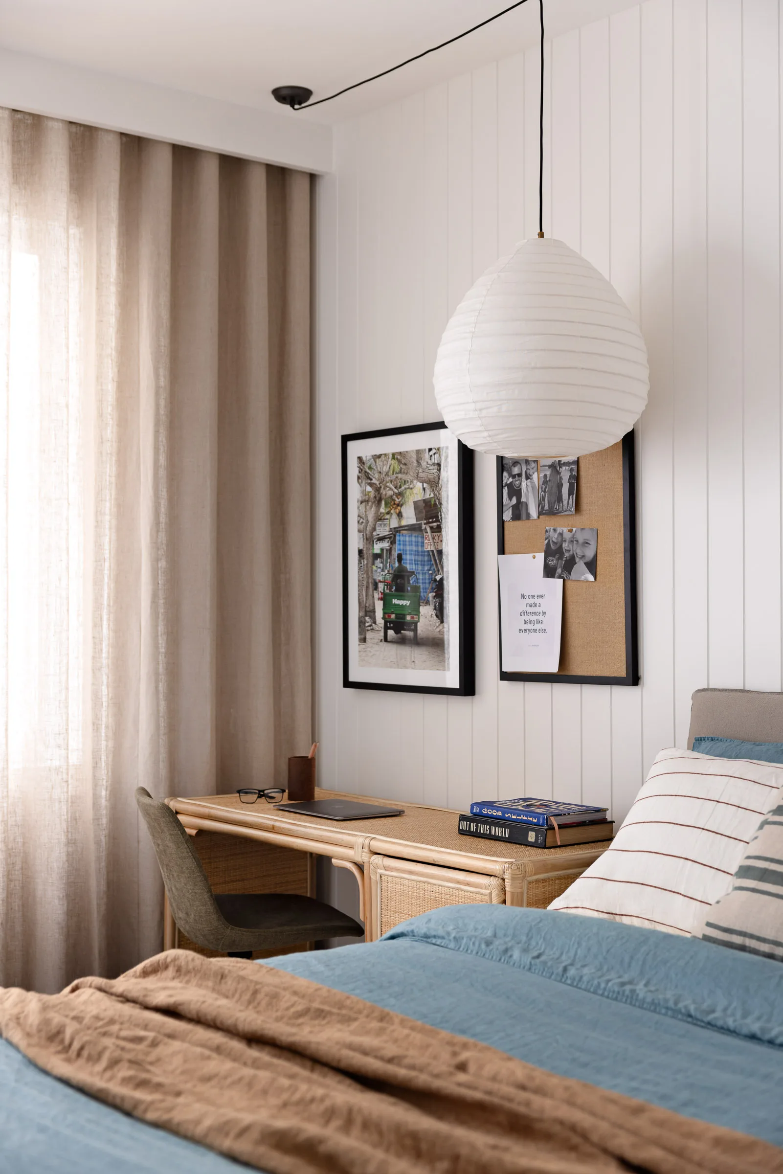 A teenager's bedroom with dark blue linen sheets, a paper pendant light and a rattan desk