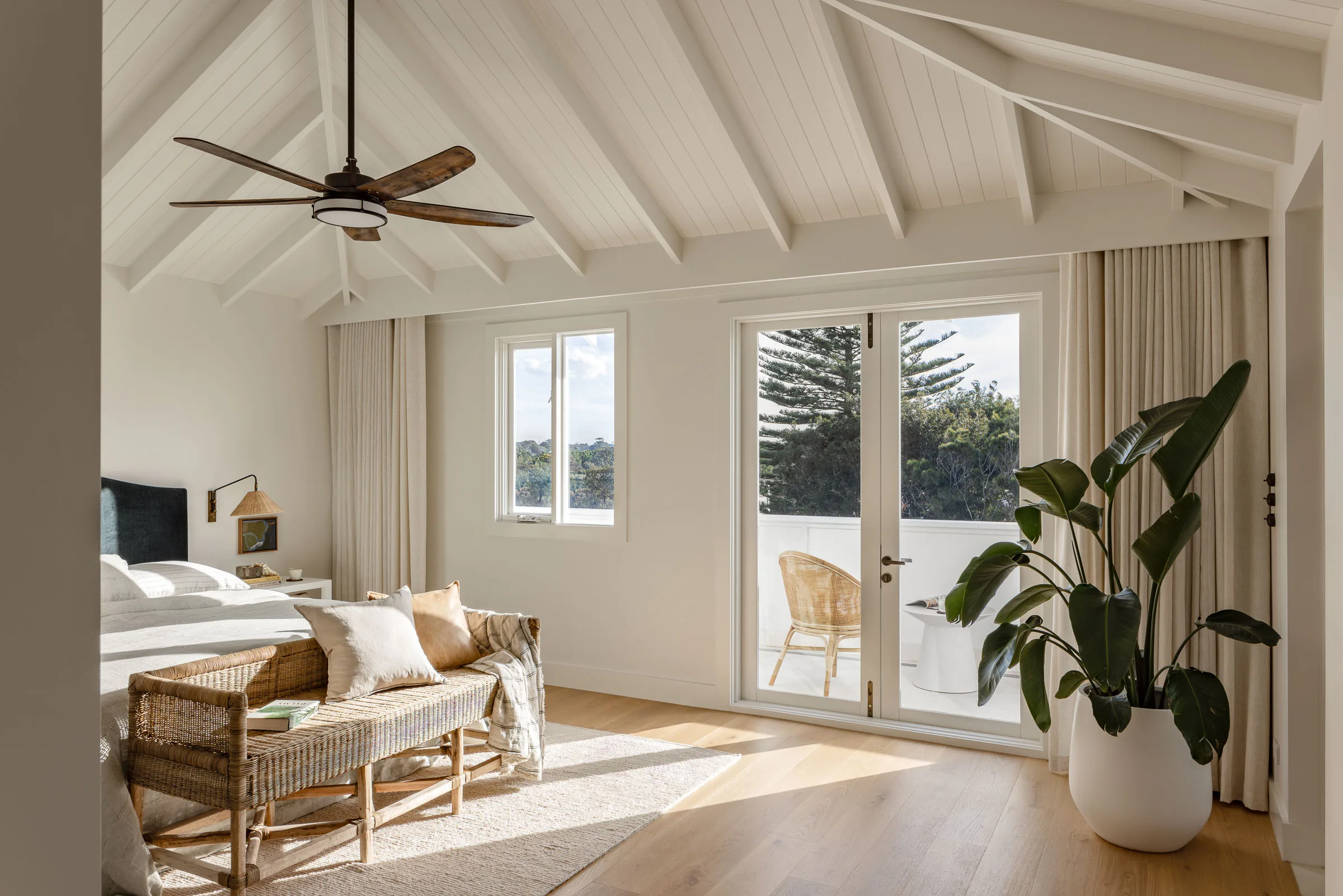 A master bedroom with white walls and a dramatic pitched roof with exposed beams